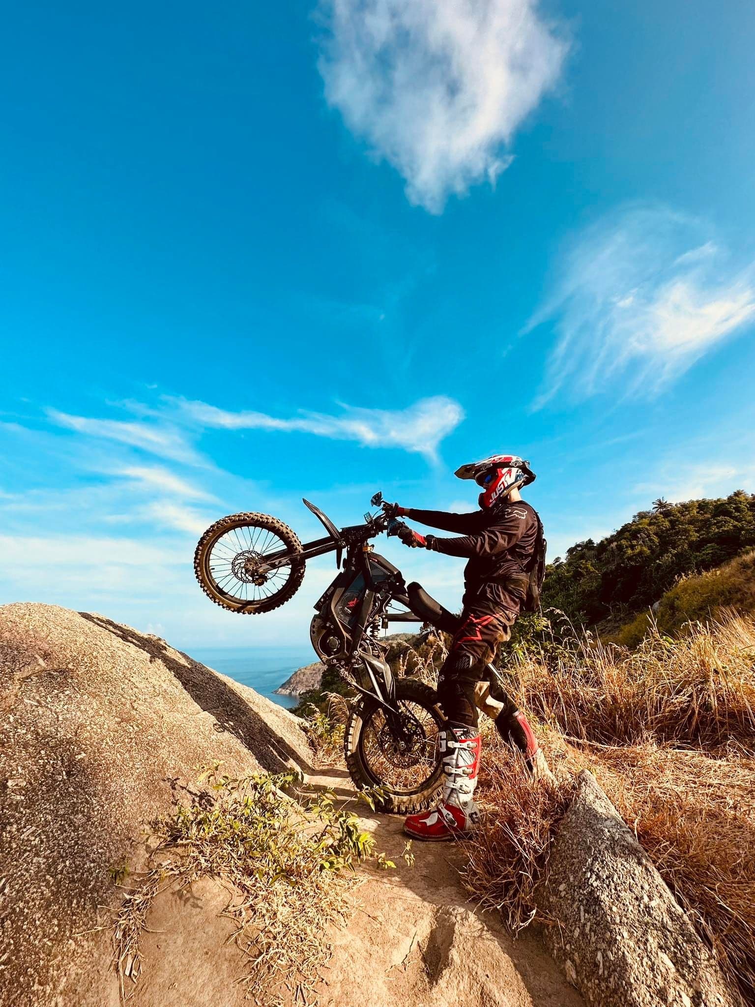A rider performing a wheelie on an electric motorbike in a scenic outdoor setting.