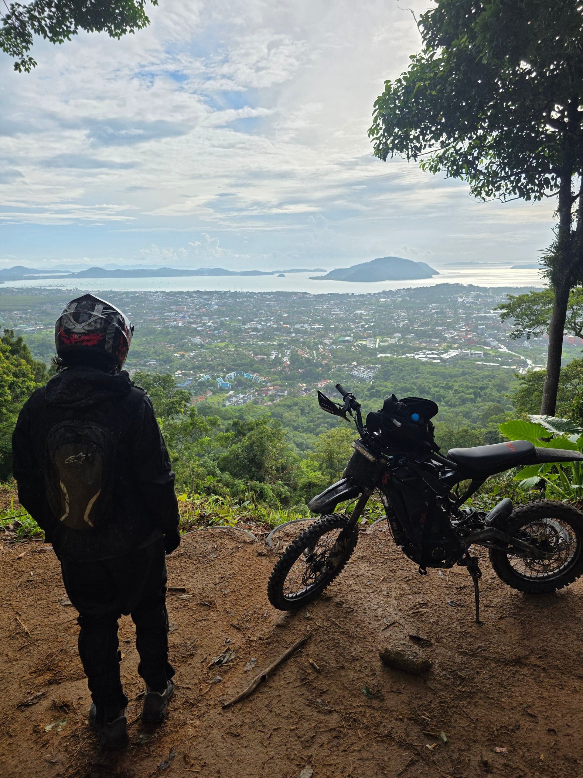 A person standing next to an electric motorbike overlooking a scenic Phuket view.